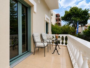 A balcony with two chairs and a table, a potted plant, and a flag.