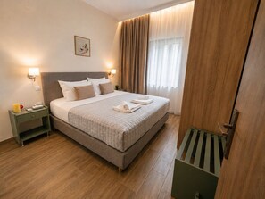 Ein ordentlich eingerichtetes Hotelzimmer mit einem großen Bett, Nachttischlampen, einem Beistelltisch und einem Fenster mit Vorhängen.