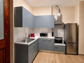 Eine kleine Küche mit grauen Schränken, einem Edelstahl-Kühlschrank, einer Mikrowelle, einem Herd und einem Spülbecken.