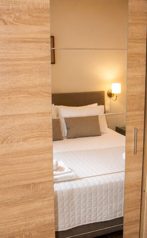 A hotel room with a bed, pillows, a nightstand, and a wall-mounted lamp.
