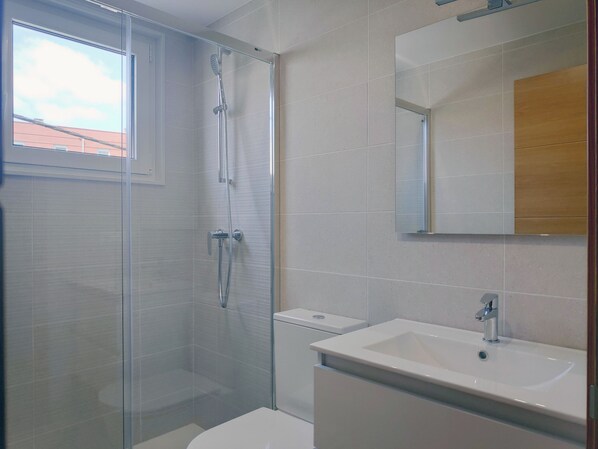 Uma casa de banho moderna com chuveiro em cabine de vidro, sanita branca e lavatório com espelho em cima.