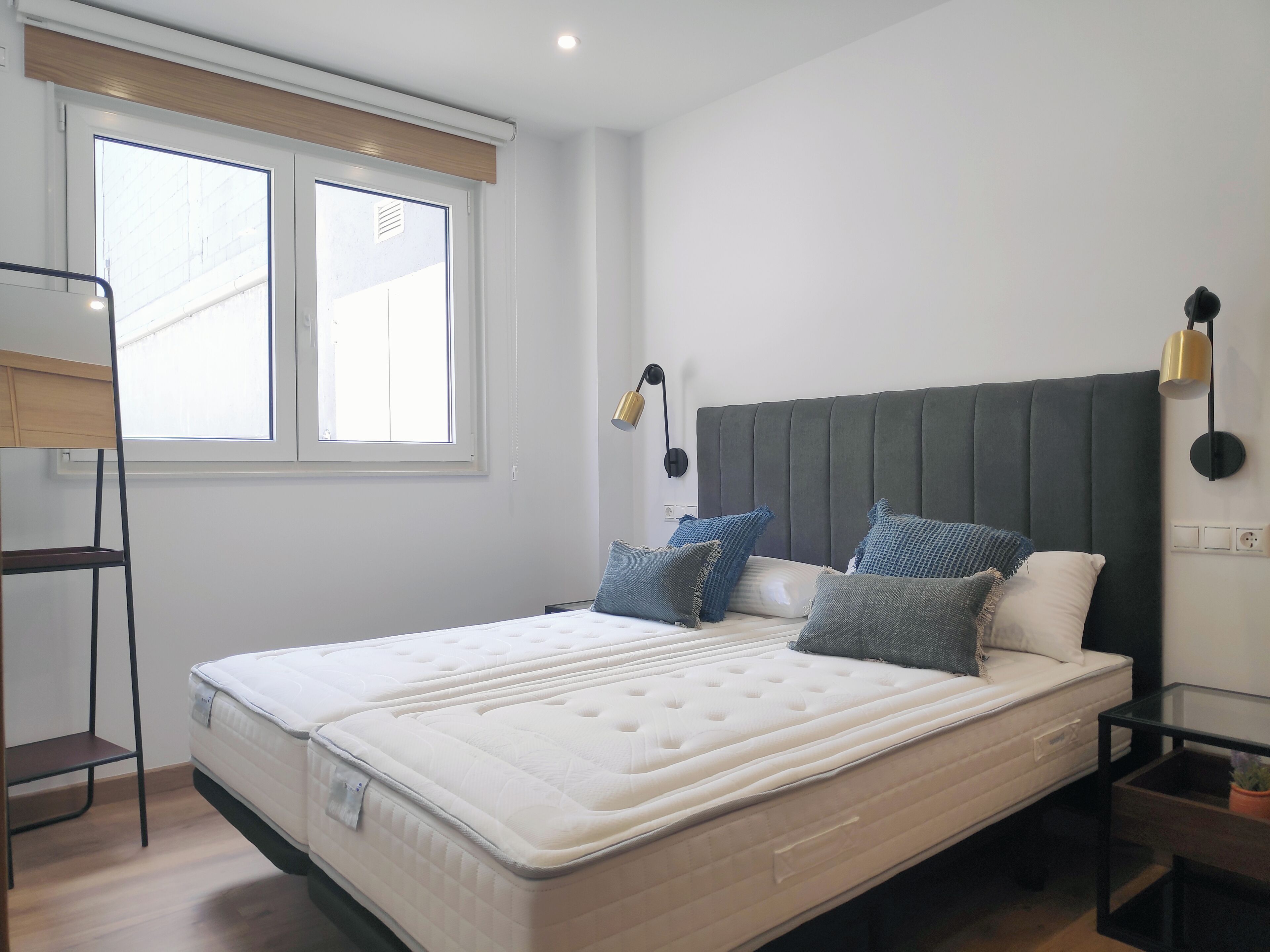 A bedroom with a large bed, two bedside lamps, a nightstand, and a window with blinds.