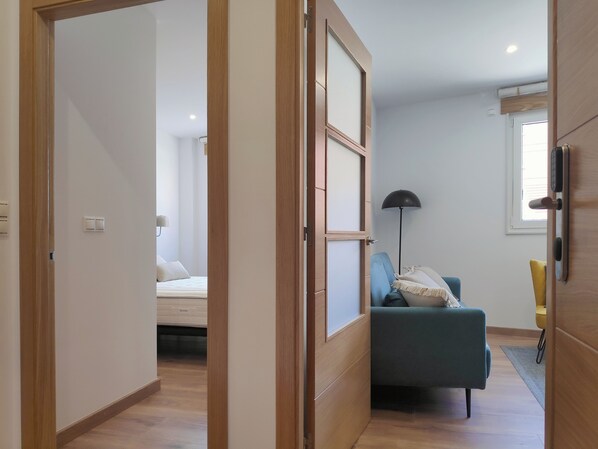 A modern bedroom with a bed, a blue sofa, a floor lamp, and a window with blinds. - Apartamentos Rey (Santiago de Compostela)