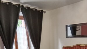 A bedroom with a bed, curtains, a window, a radiator, and a mirror on the wall. - Les randonneurs room  (Aydat)