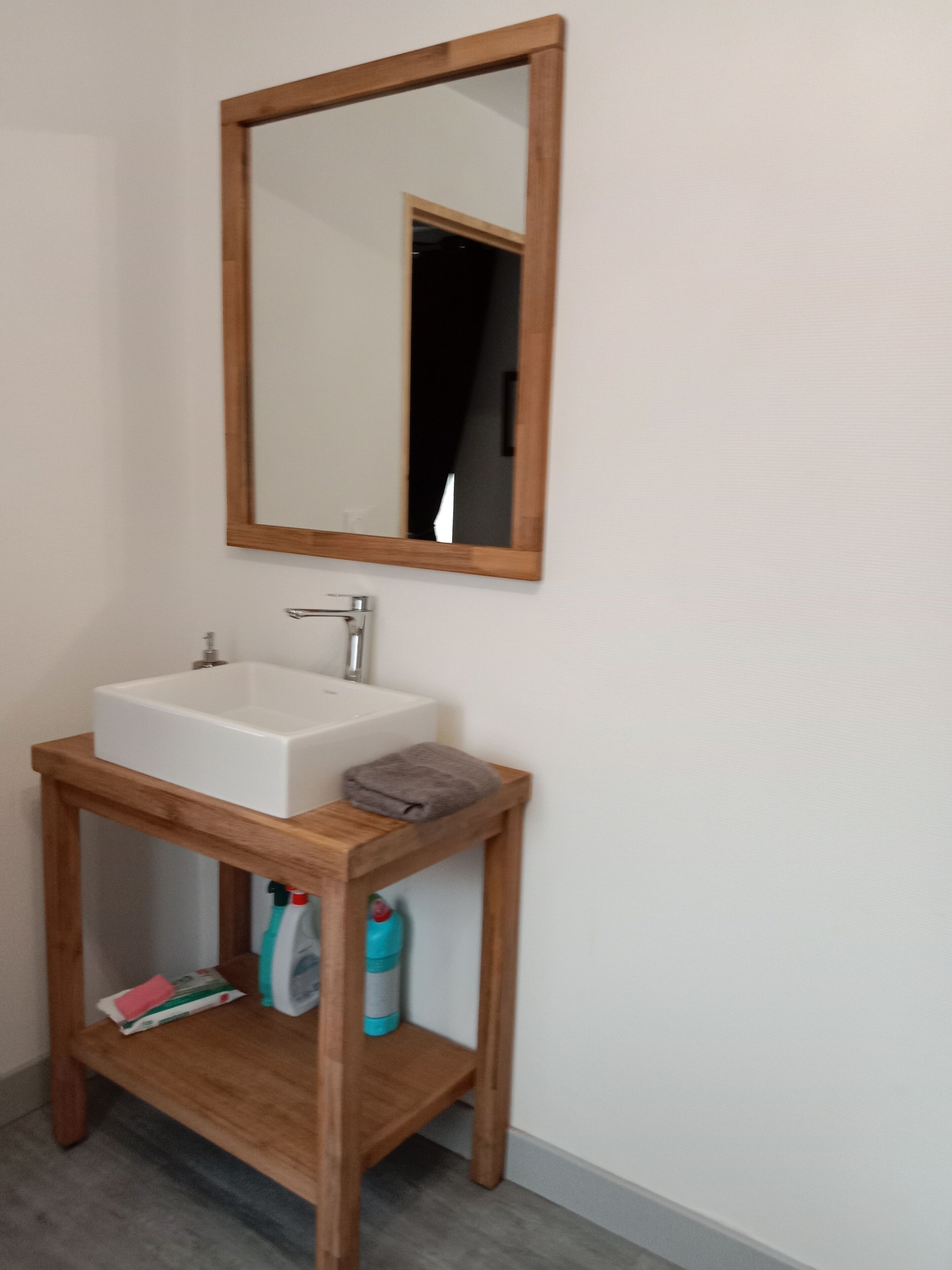 Een badkamer met een houten wastafel, een witte wasbak en een spiegel erboven.