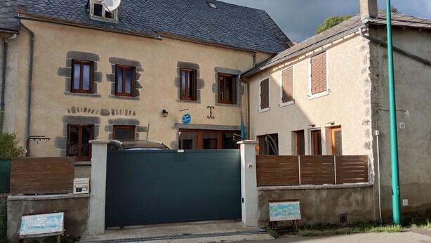 A two-story building with a large garage door, stone facade, and multiple windows with shutters. - Les randonneurs room  (Aydat)