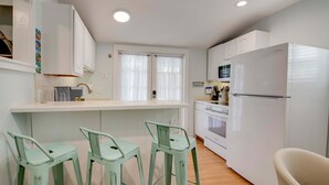 A modern kitchen with white cabinets, a stainless steel refrigerator, and a wooden countertop. There are three green stools and a white chair. - New The Cottage at James House (Key West)