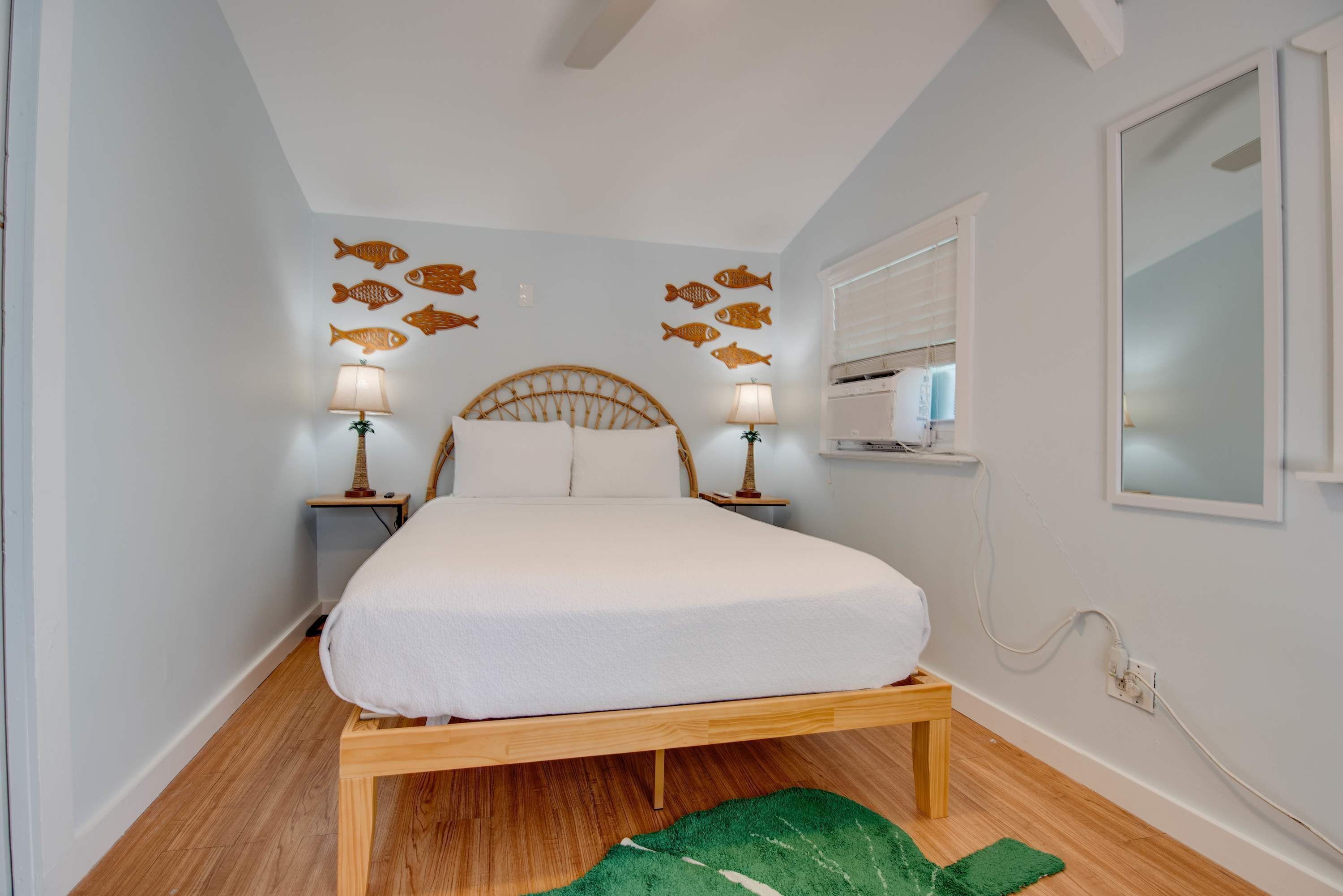 A bedroom with a wooden bed, two bedside tables with lamps, and wall decorations of fish.
