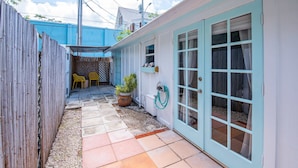 A narrow outdoor patio with a tiled floor, a wooden fence, and a blue building with a white door. - New The Cottage at James House (Key West)