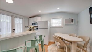 A compact kitchen with white cabinets, a refrigerator, a microwave, and a dining area with a table and chairs. - New The Cottage at James House (Key West)