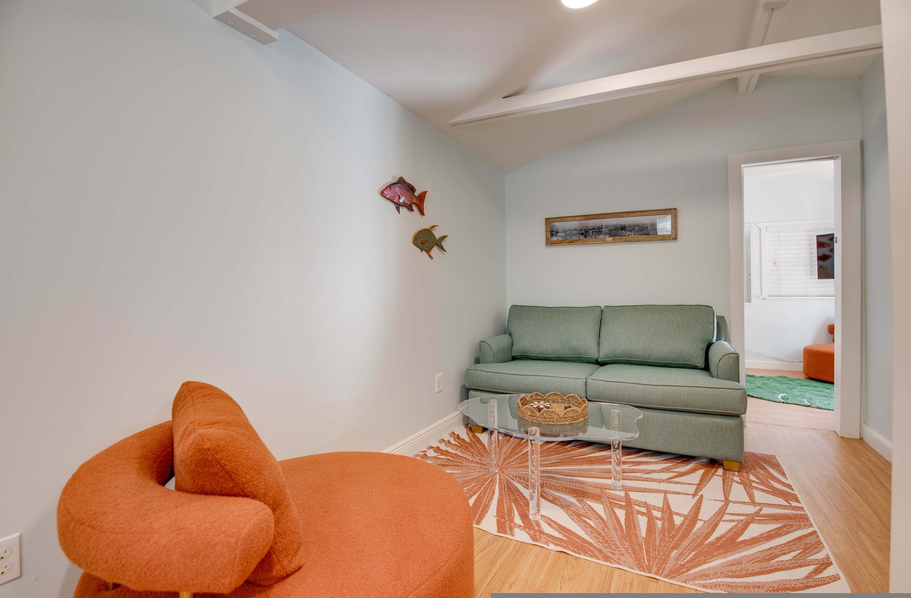 Ein modernes Wohnzimmer mit einem grünen Sofa, einem orangefarbenen Sessel und einem Glastisch.