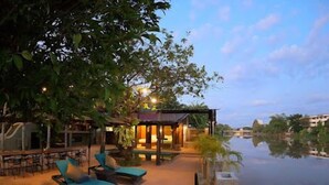 A serene outdoor area with lounge chairs and a pool, surrounded by lush greenery and a calm water body.