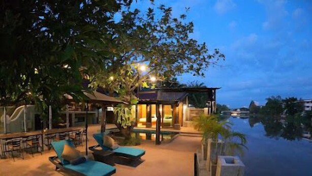 A poolside area with lounge chairs and a covered seating area, surrounded by trees and a view of the water.