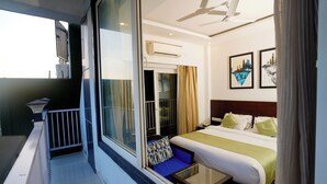 A hotel room with a balcony, a bed with green and white bedding, a small table, and two framed pictures on the wall. - N3N Ganga Retreat by Stotrak (Rishikesh)