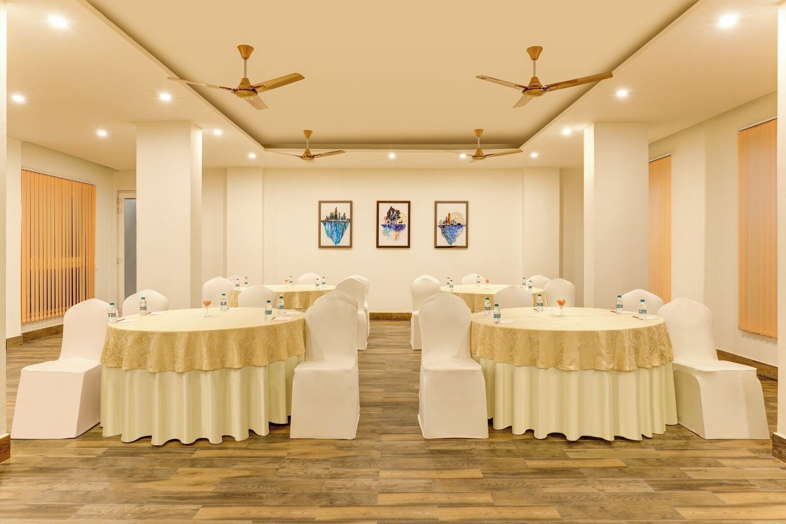 A conference room with round tables, white chairs, ceiling fans, and artwork on the walls.