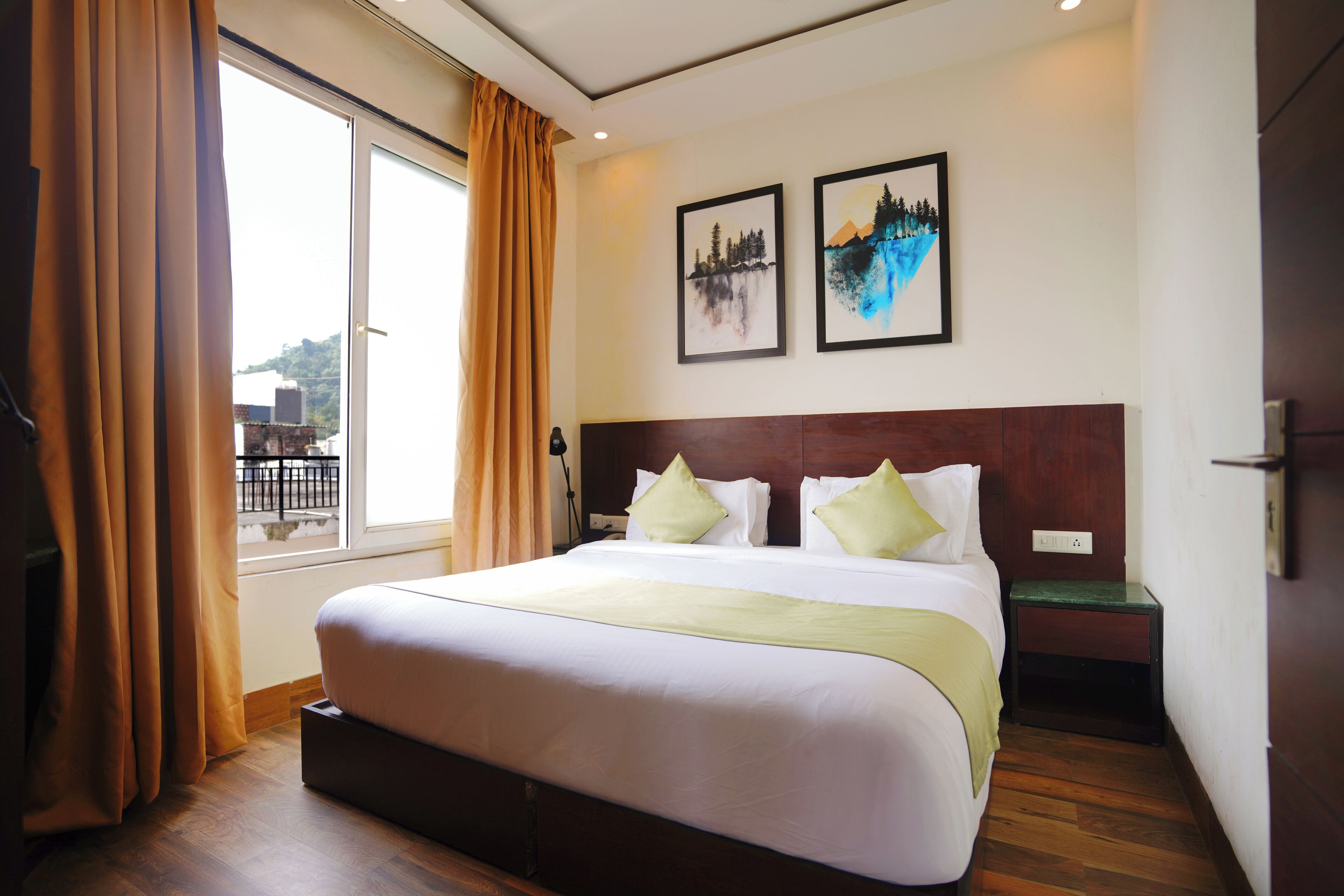 Una habitación de hotel con una cama grande, suelo de madera, dos obras de arte en la pared y una ventana con cortinas.