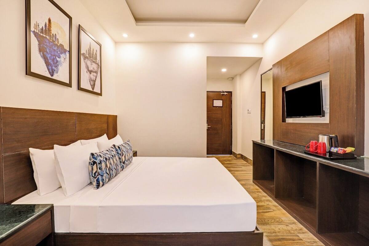 A hotel room with a large bed, a TV mounted on the wall, and a wooden headboard.
