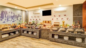 A buffet area with various food stations, including a bread station, a pickles station, and a pancake station. There are also several wall-mounted plates and a flat-screen TV. - N3N Ganga Retreat by Stotrak (Rishikesh)