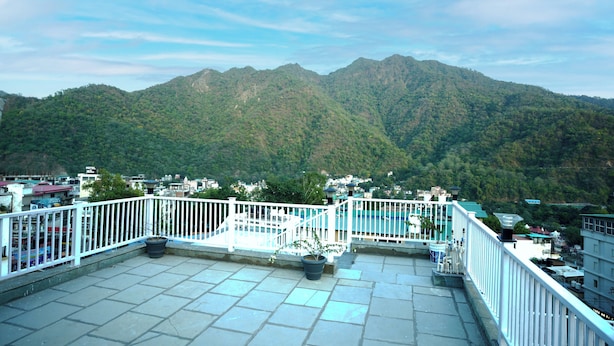 A rooftop terrace with a view of a mountain range, white railings, and potted plants. - N3N Ganga Retreat by Stotrak (Rishikesh)