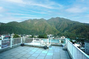 Una terraza en la azotea con vistas a una cordillera, barandillas blancas y plantas en macetas.