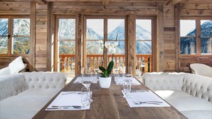Una habitación con paneles de madera, una gran mesa de comedor dispuesta para dos personas, una orquídea en maceta y vistas a la montaña a través de amplios ventanales.