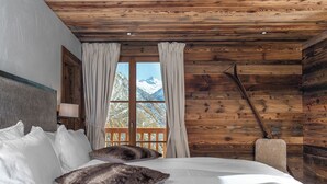 Un dormitorio de cabaña de madera con una cama, almohadas, una mesita de noche y una ventana con cortinas.