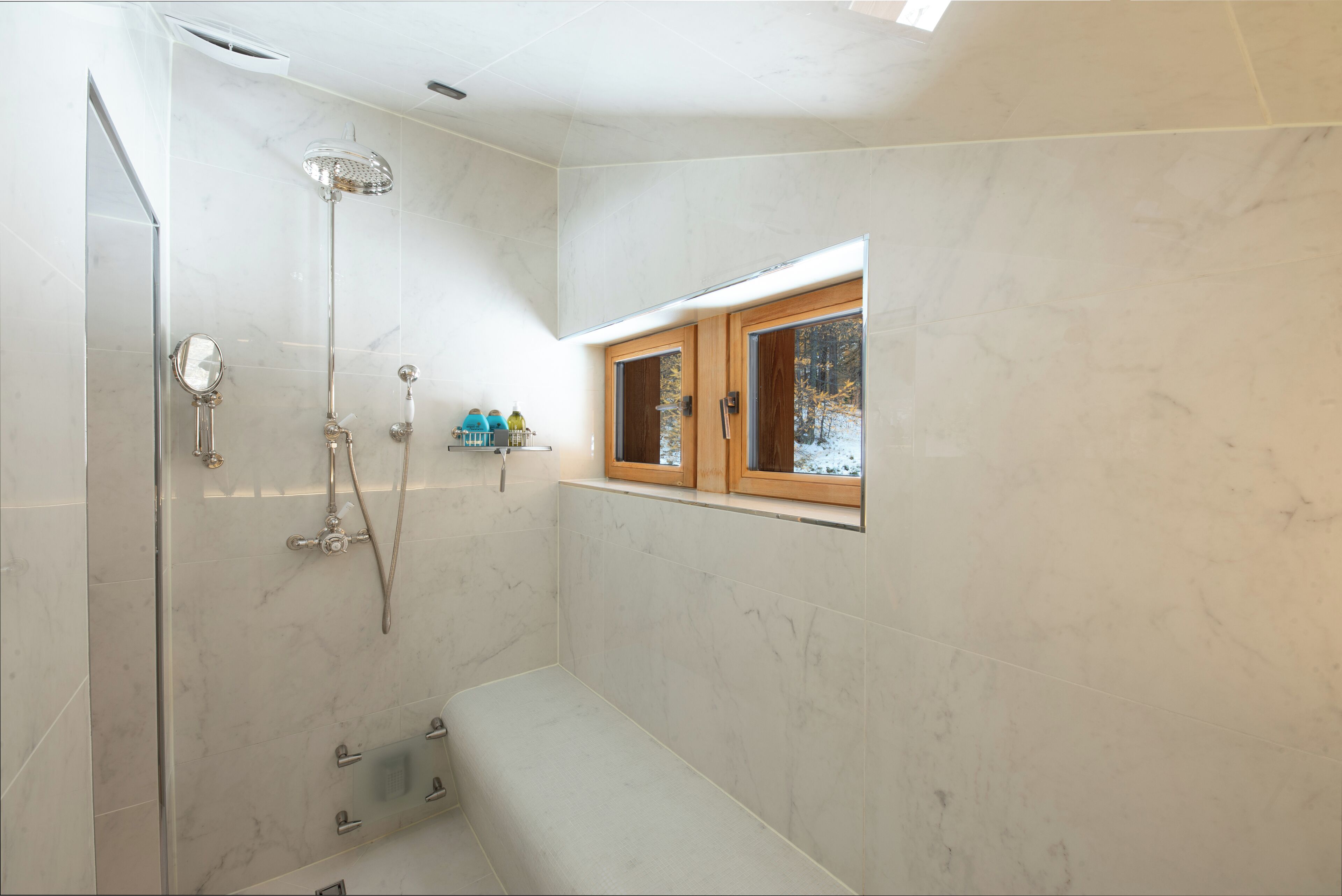 Un baño moderno con ducha acristalada, banco integrado y ventana con vistas a árboles.