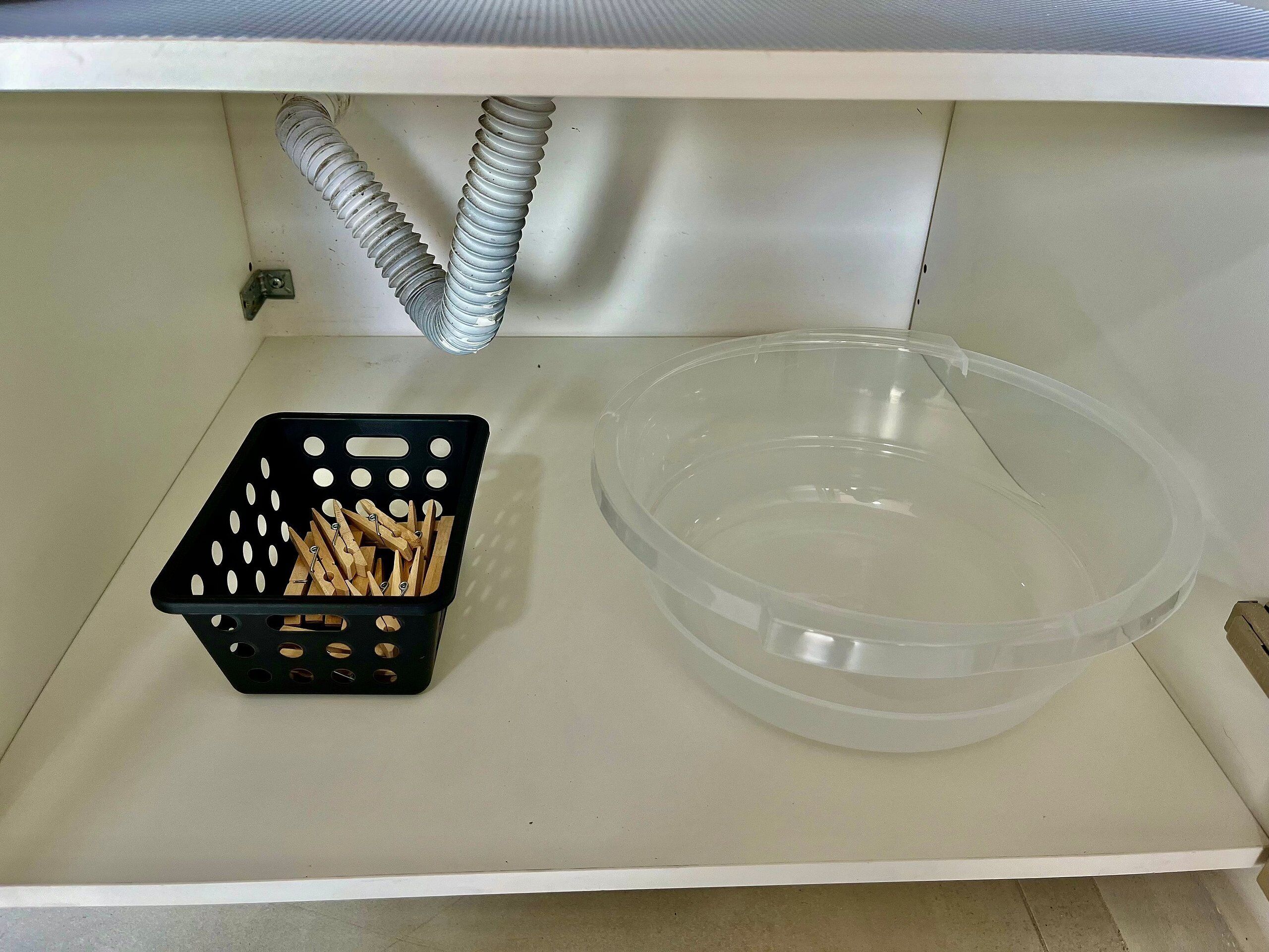 A white shelf with a black basket containing wooden clothespins and a clear plastic container.