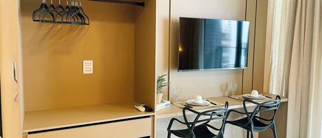 A hotel room with a wardrobe, a dining area with a table set for two, and a TV mounted on the wall.