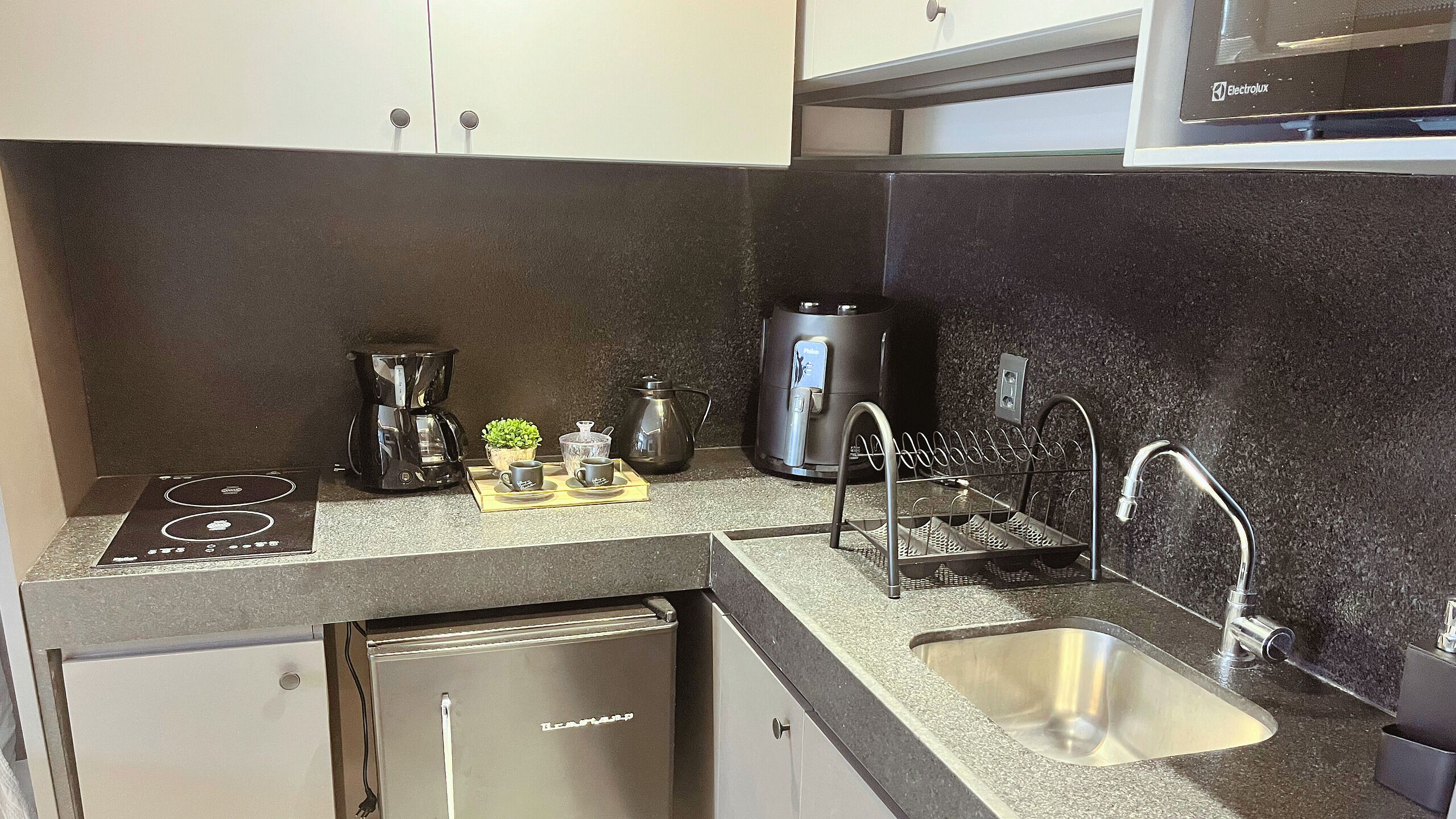 A compact kitchenette with a coffee maker, kettle, and a small potted plant.
