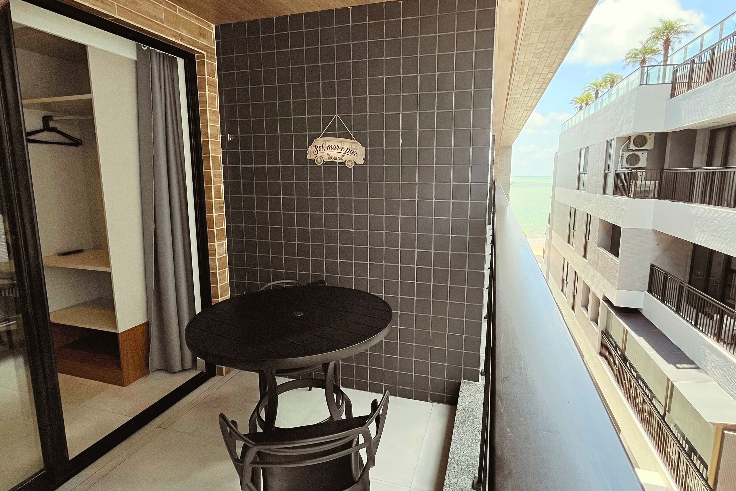 Un balcone con tavolo e sedie, vista sul mare e un muro piastrellato con una decorazione a forma di automobile appesa.