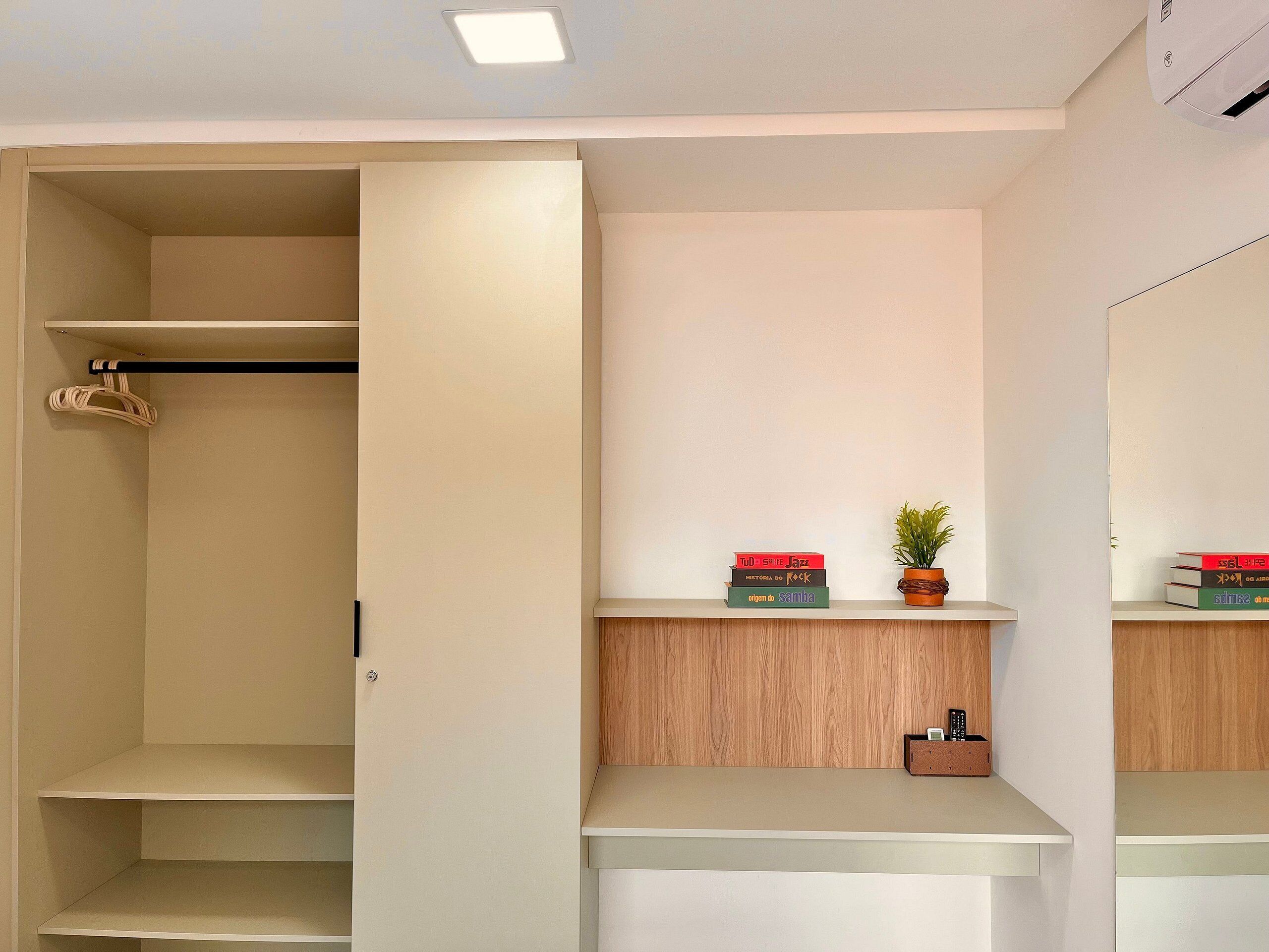A modern closet with open doors, a hanging rack, and a shelf with books and a plant.