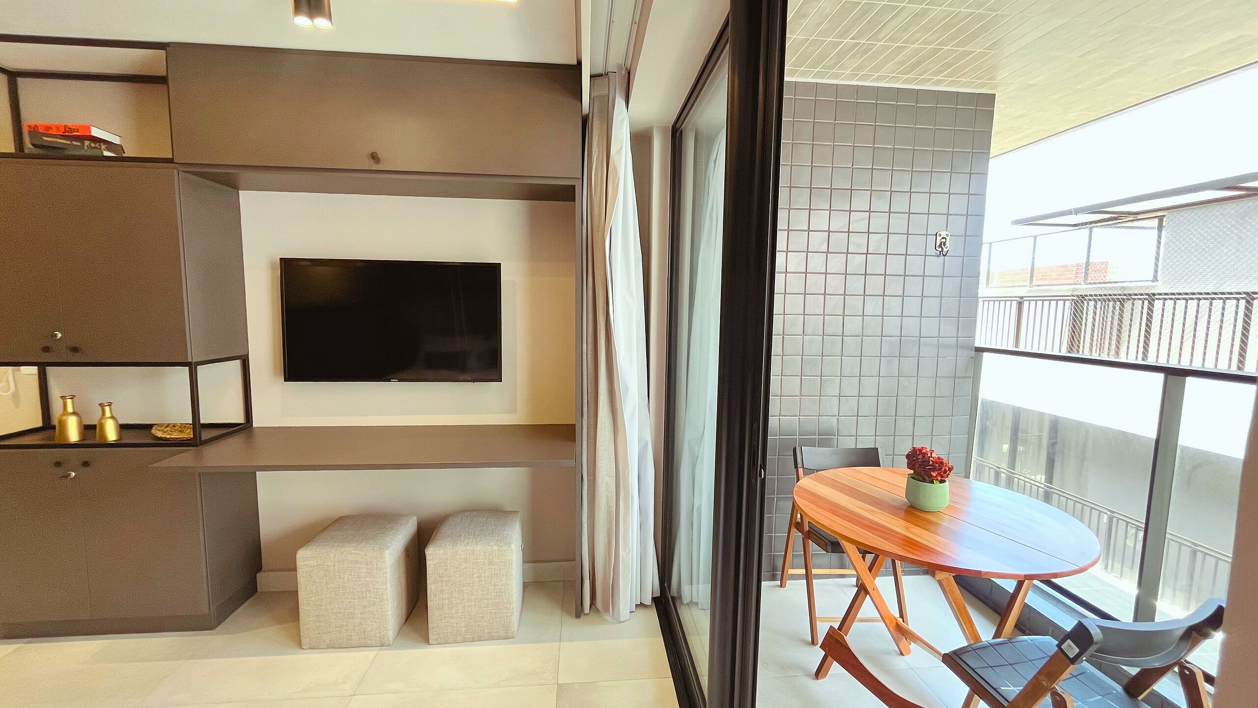 Ein modernes Wohnzimmer mit Flachbildfernseher, integrierten Regalen und einem Balkon mit Holztisch und Stühlen.