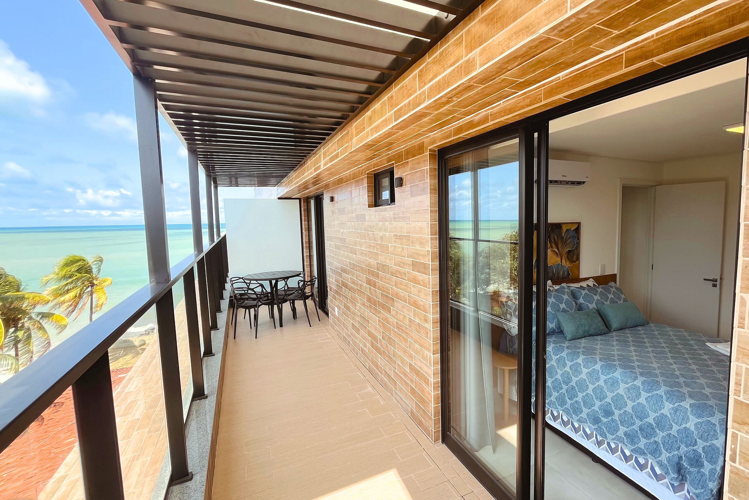 Un balcón con vistas al océano, una cama con edredón estampado y una pequeña mesa con sillas.