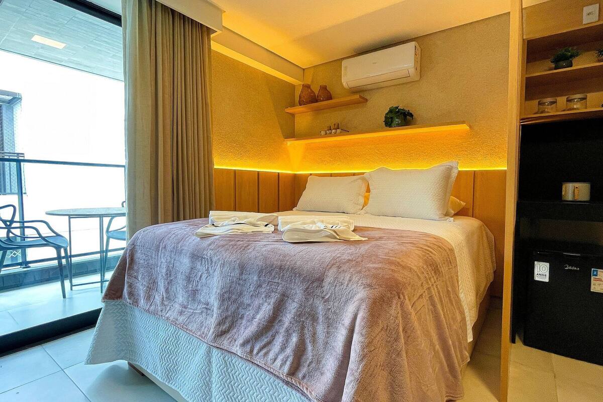 Une chambre d’hôtel comprenant un lit, une petite table avec des chaises, un appareil de climatisation et une étagère avec des objets décoratifs.