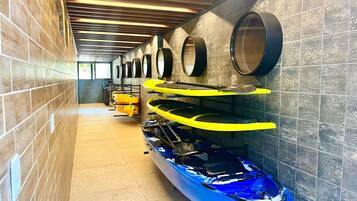 Una serie di kayak e tavole da paddleboard in un'area coperta con pareti in piastrelle e soffitto in legno.