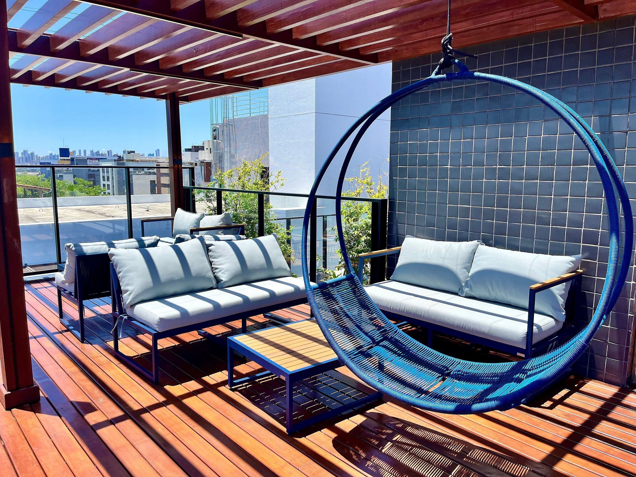Terraza en la azotea con una silla colgante, un sofá y una pequeña mesa.