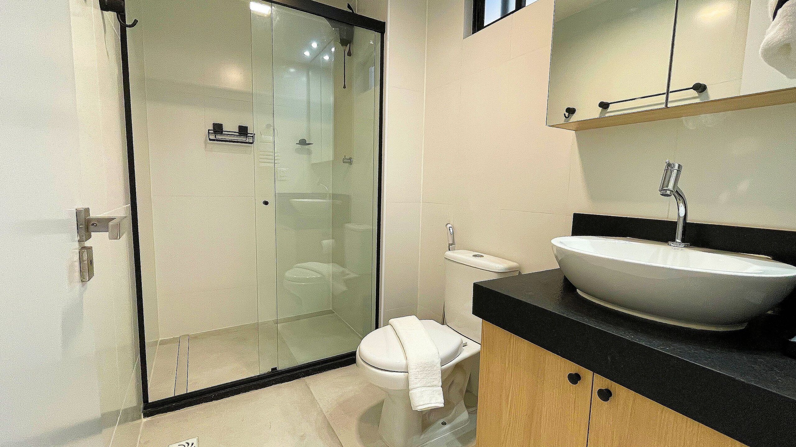 A modern bathroom with a glass-enclosed shower, a white sink, and a toilet.
