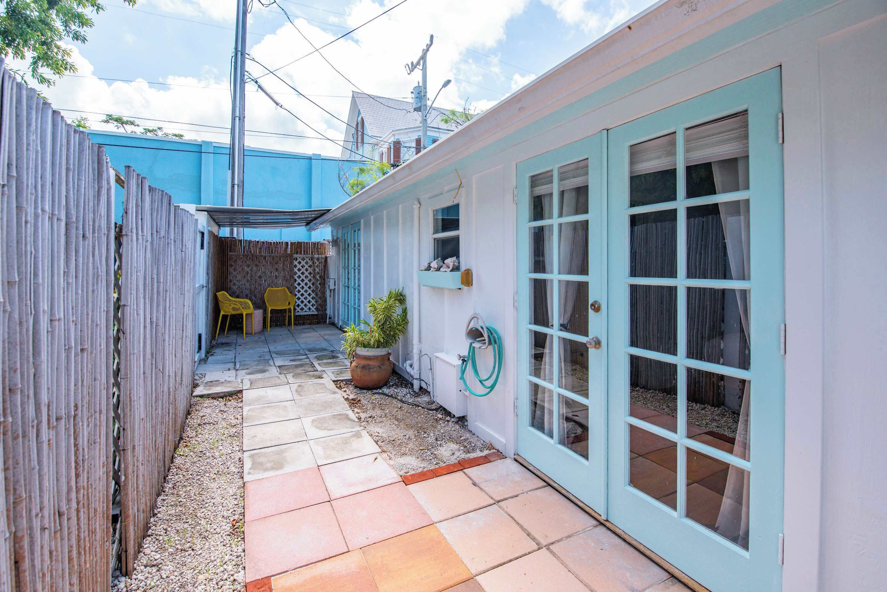Un petit patio extérieur avec un sol carrelé, une clôture en bois et un bâtiment bleu avec une porte blanche.
