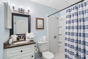 A bathroom with a sink, mirror, and toilet. There is a shower curtain and a framed picture on the wall. - Plantation 2118 with Pool (Gulf Shores)