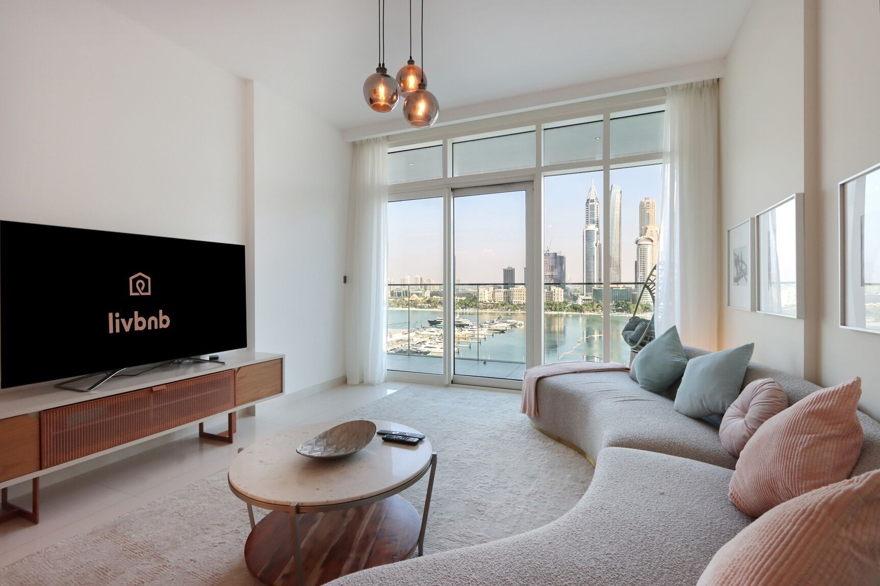 Ein modernes Wohnzimmer mit großem Flachbildfernseher, einer Couch, einem Couchtisch und einem Balkon mit Blick auf die Stadt.