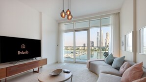 A modern living room with a large flat-screen TV, a sofa, a coffee table, and a balcony with a city view. - 2BR Beachfront Living, Stunning Marina Views (Dubai)
