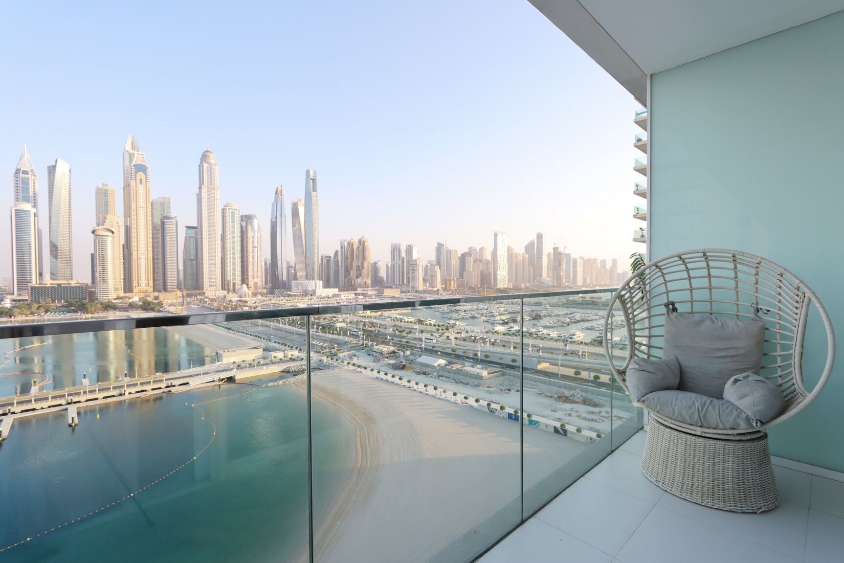A balcony with a view of a city skyline, a swimming pool, and a wicker chair.