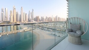 A balcony with a view of a city skyline, a swimming pool, and a wicker chair. - 2BR Beachfront Living, Stunning Marina Views (Dubai)