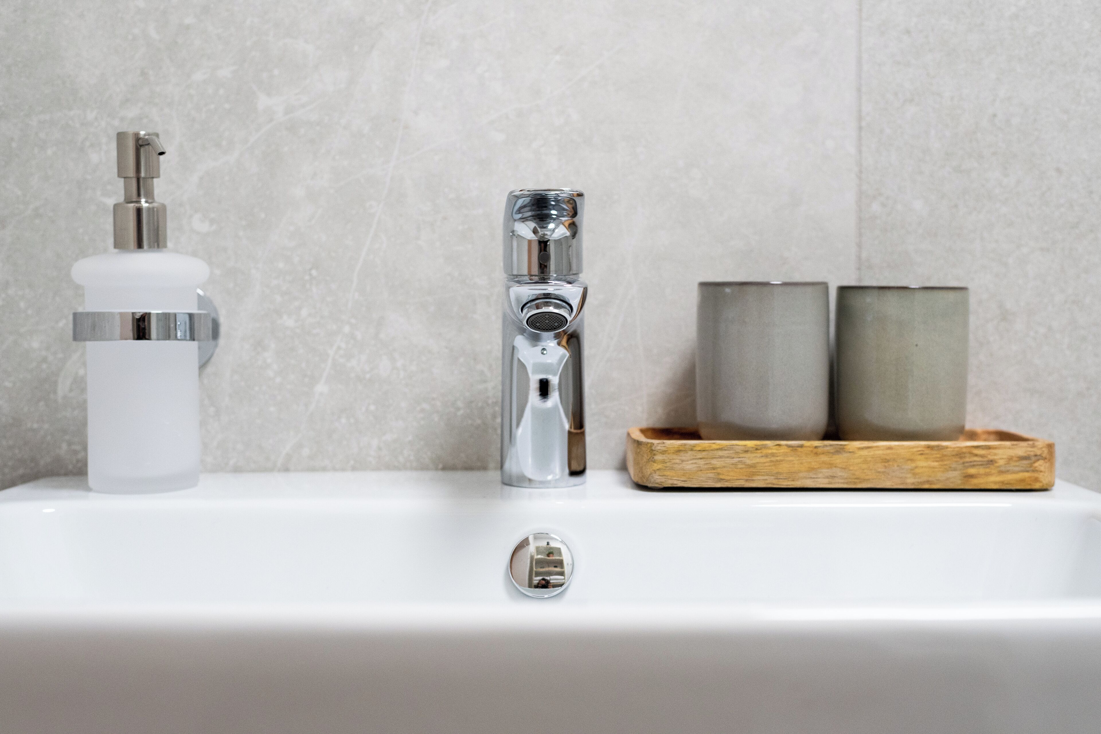 A bathroom sink with a chrome faucet, a soap dispenser, and two candles in a wooden holder.