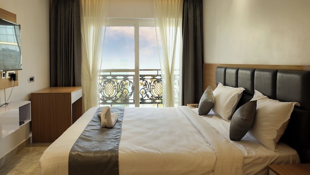 A hotel room with a large bed, a wooden nightstand, a TV mounted on the wall, and a balcony with a view. - Hacana Millenium Hotel (Hyderabad)