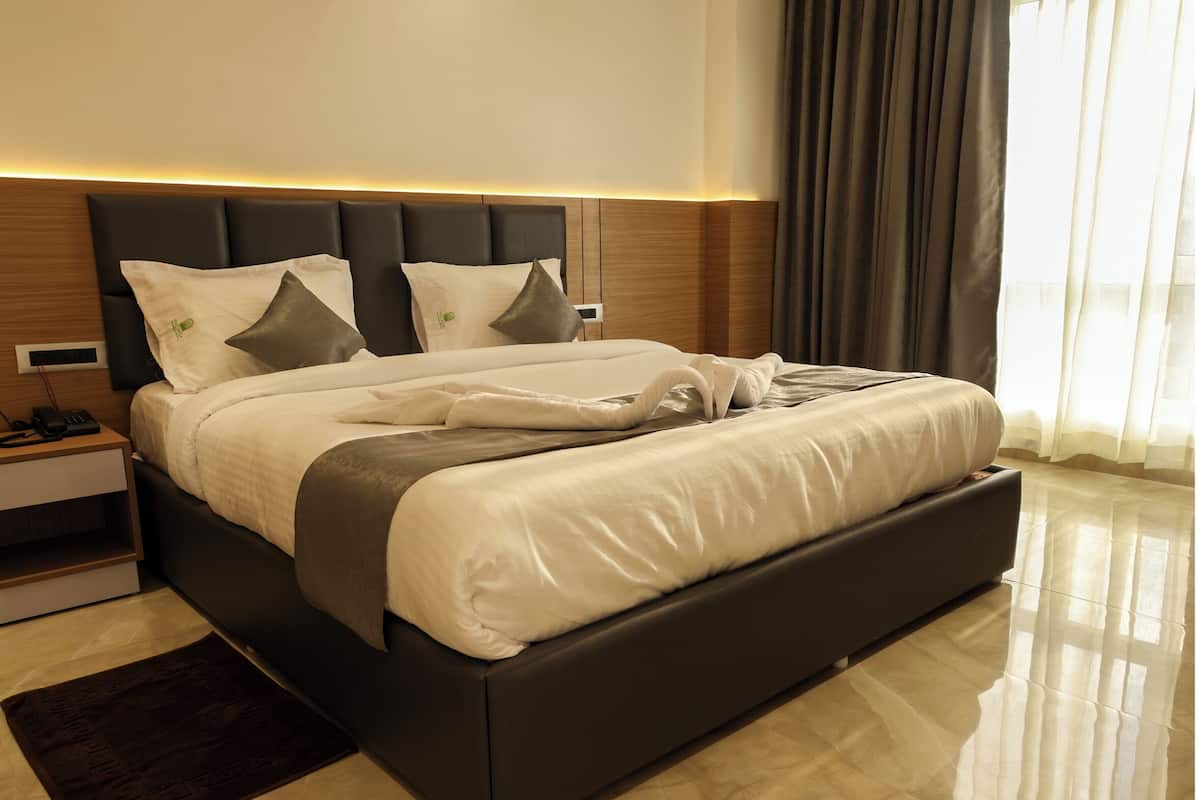 A modern hotel room with a large bed, a wooden headboard, a bedside table with a phone, and a nightstand.