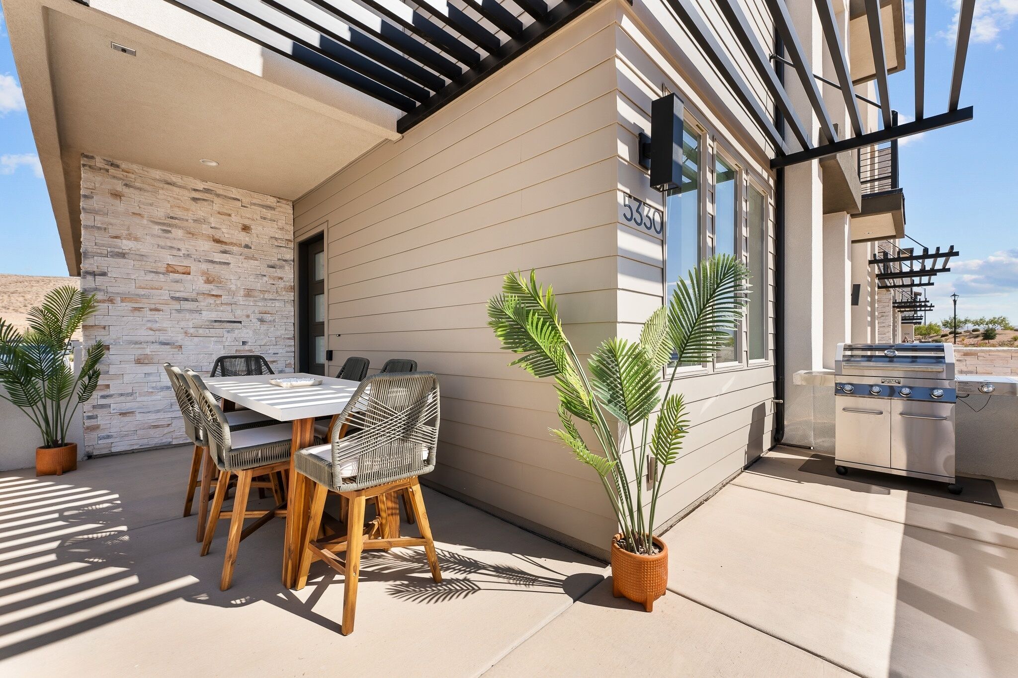 An outdoor patio with a dining table and chairs, a grill, and potted plants.
