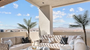 Eine Dachterrasse mit einem beigefarbenen Sofa, gestreiften Kissen und zwei Palmen.