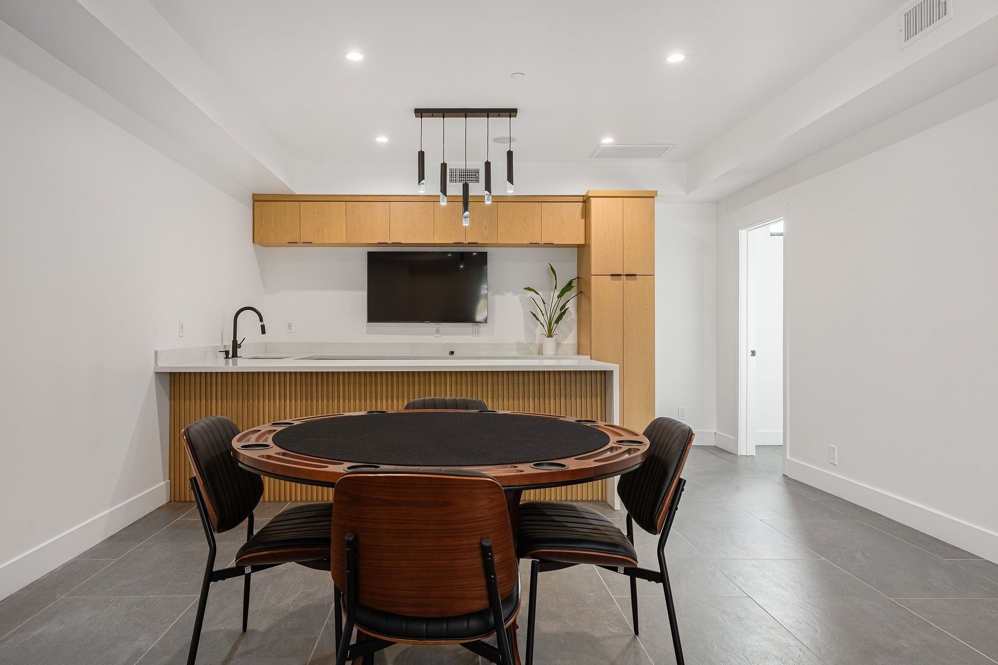A modern kitchen with wooden cabinets, a built-in TV, and a round dining table with chairs.